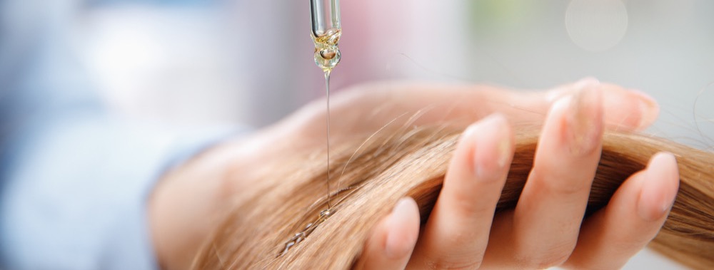 Frau hält Haare in der Hand und eine Pipette mit Arganoel - Haarpflege